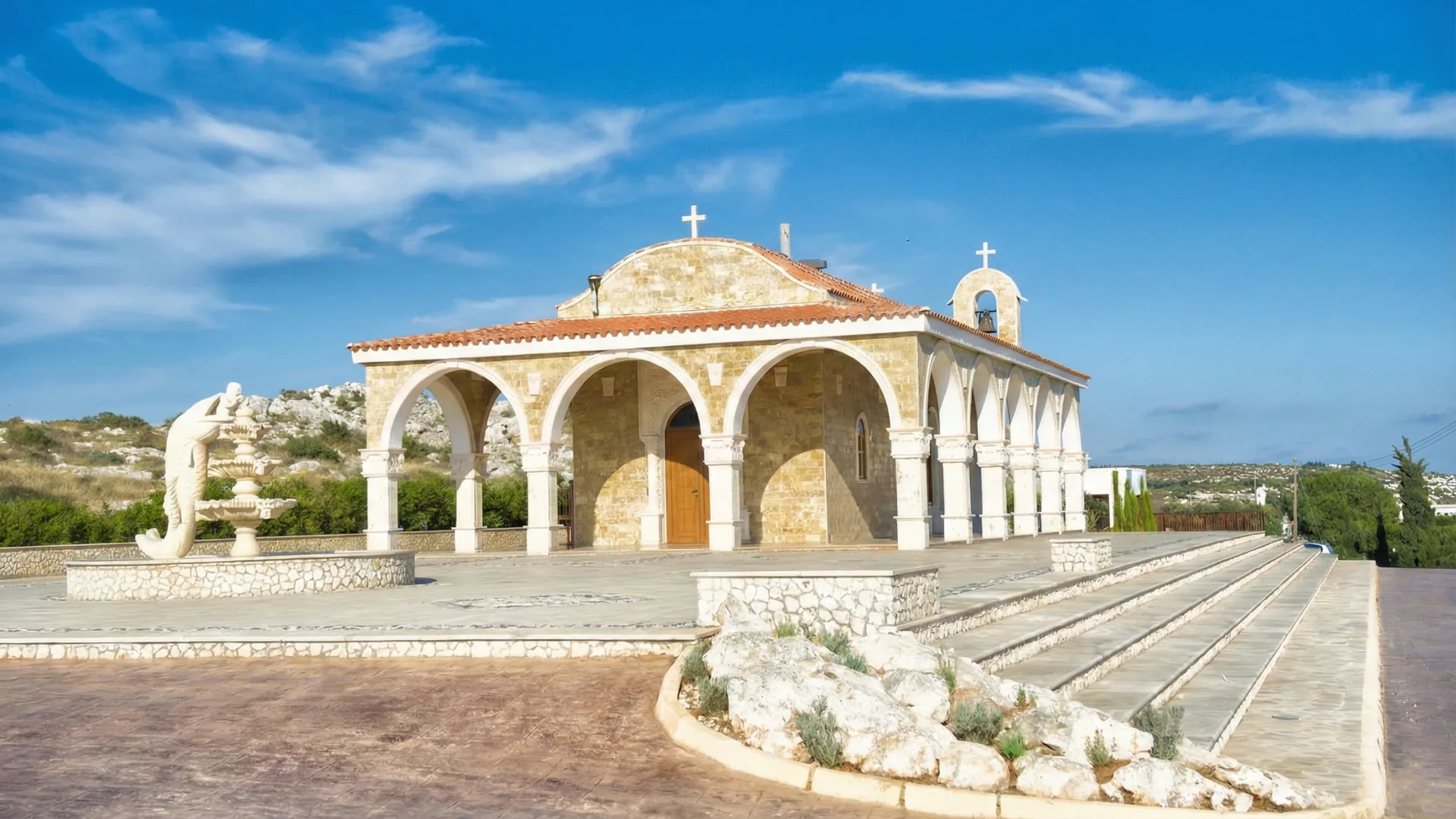 Ayios Epiphanios stone church in Cyprus with arched colonnade and bell tower, a traditional Orthodox wedding venue under a clear blue sky