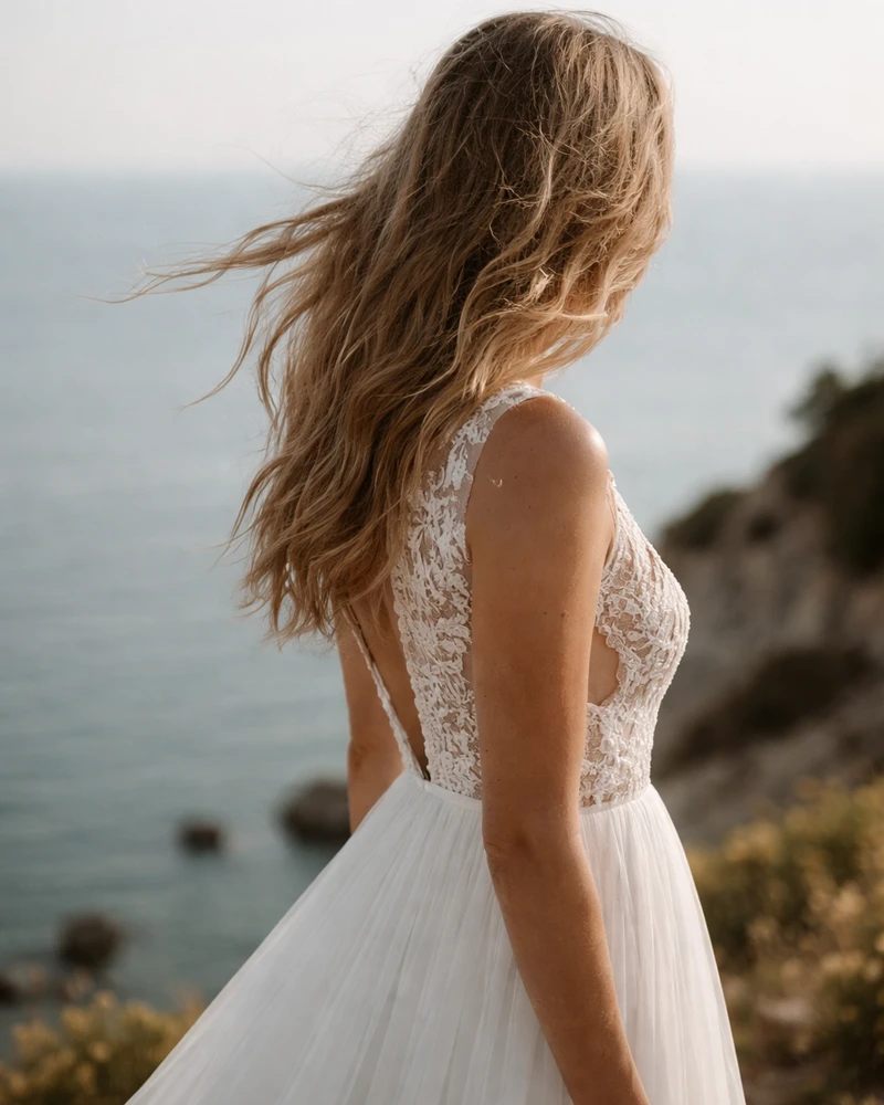 Bride in a lace wedding dress looking toward the sea on a Mediterranean clifftop.