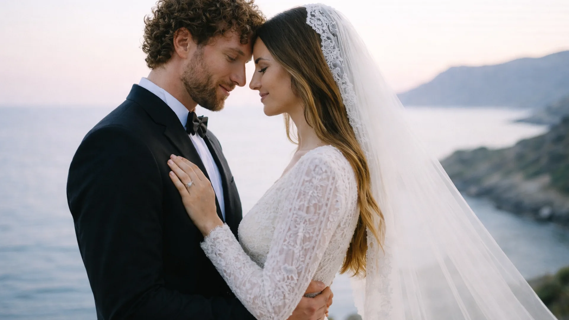 Bride and groom embracing on a seaside cliff at sunset, with flowing veil and soft golden light overlooking the ocean